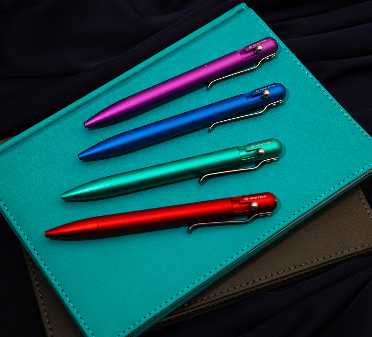 Bastion bolt action pens on a notebook, with the bolt mechanisms facing up