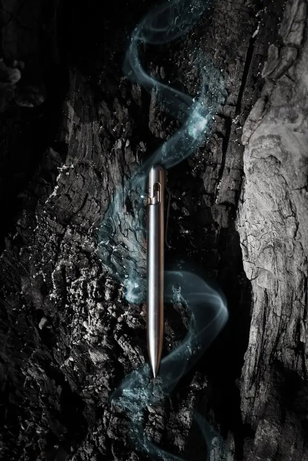 Bastion steel bolt action pen against dark bark with a soft blue wisp